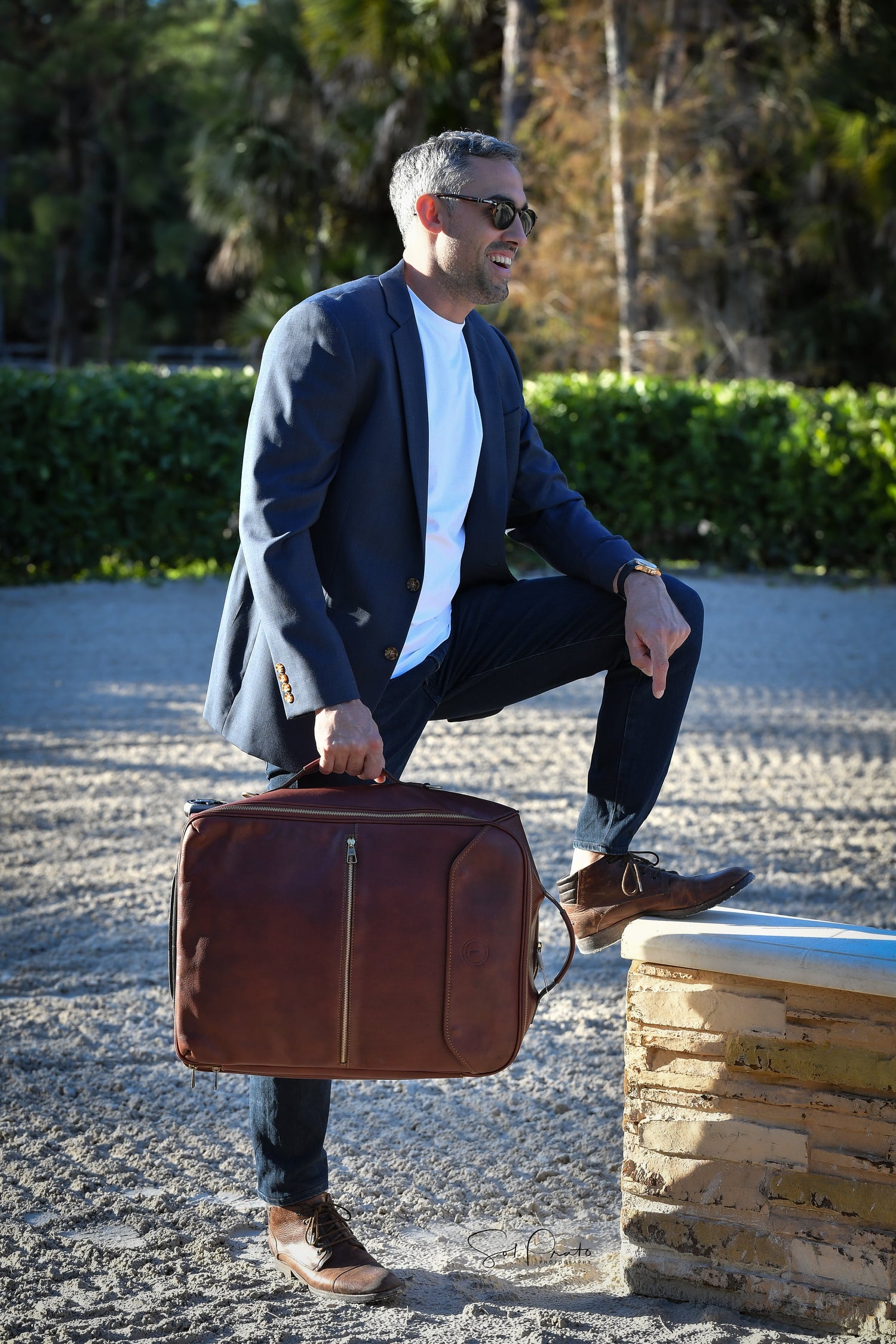 Man in blue blazer holding a brown vegetable-tanned leather briefcase by CABRERA, outdoors in natural light. The image showcases luxury and craftsmanship.